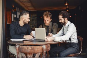 Three business professionals discussing How AI Is Changing Digital Marketing strategies around a laptop, representing AI-driven digital marketing, online growth, and modern business collaboration.